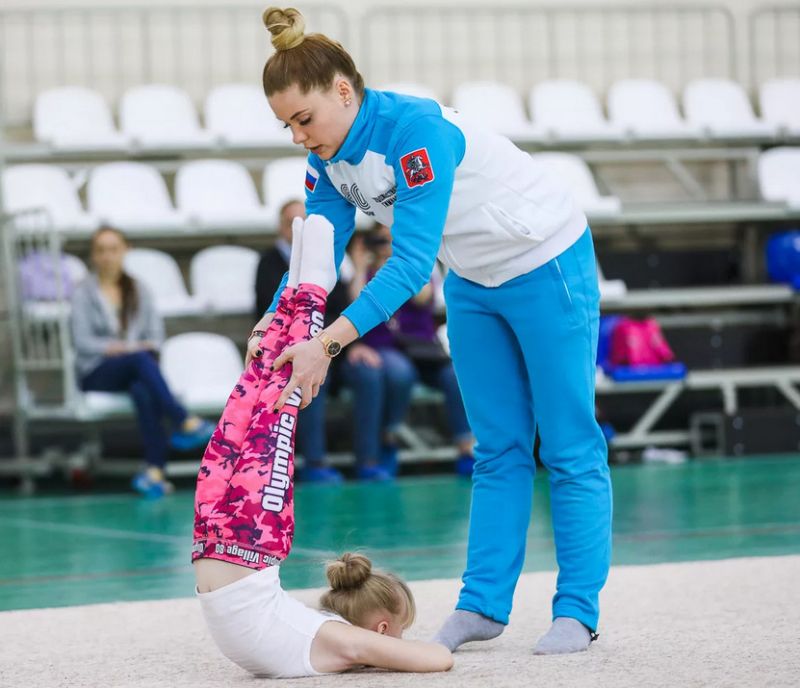 Девочка выполняет элемент гимнастики с поддержки тренера